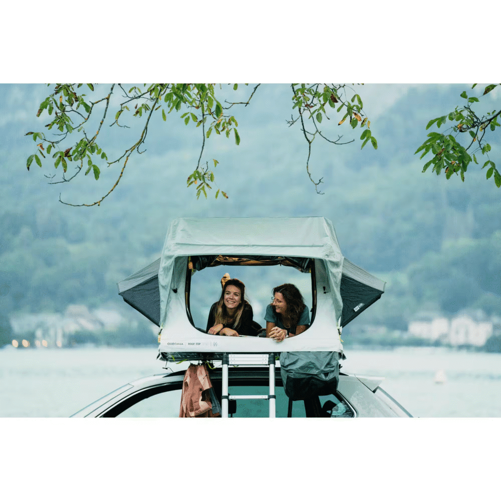 Tente de toit Quechua MH500 Fresh & Black montée sur une voiture, avec deux campeuses profitant de la vue au bord d’un lac